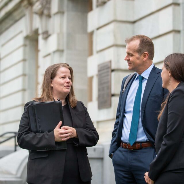 3 people in suits talking outside of courthouse