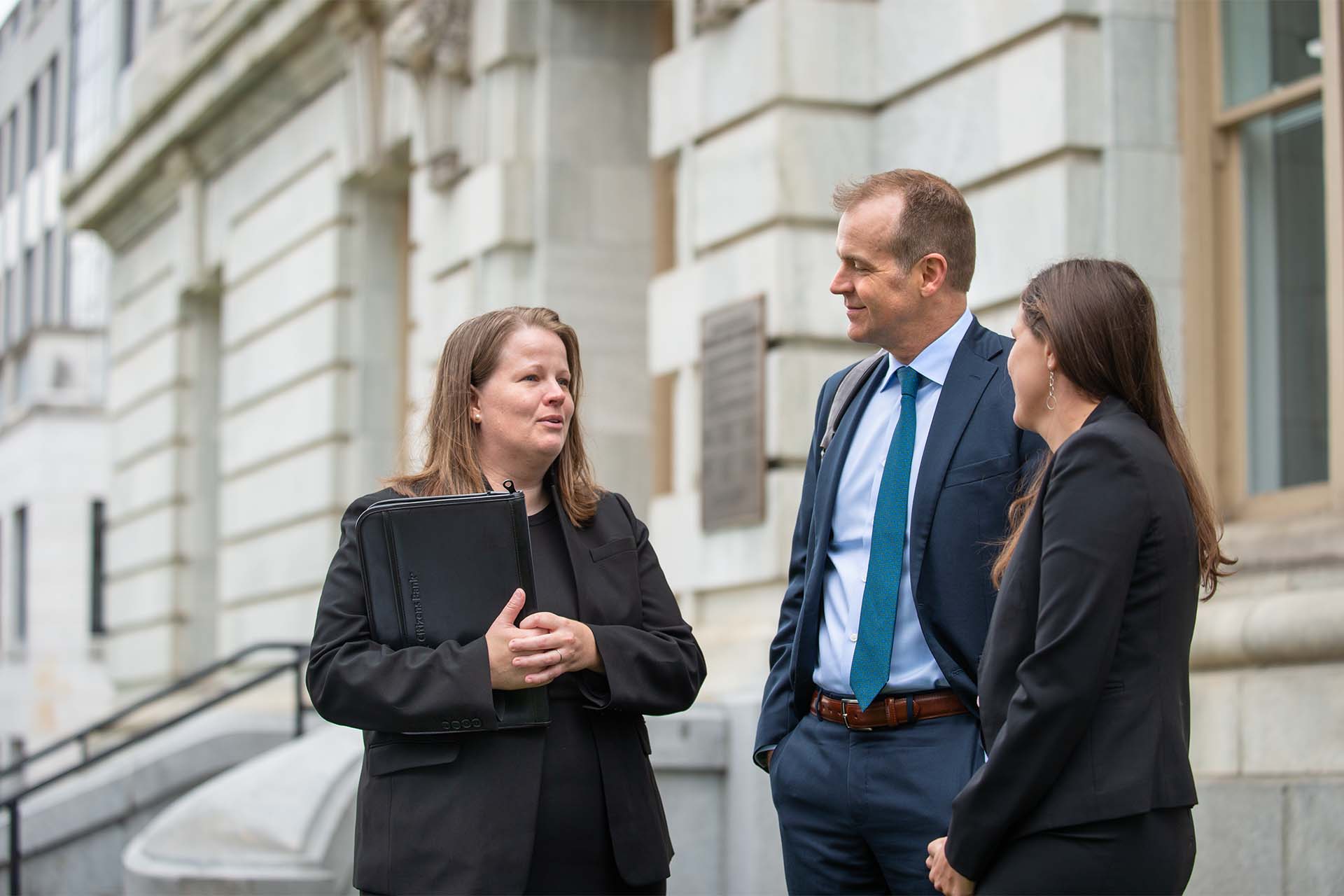 3 people in suits talking outside of courthouse