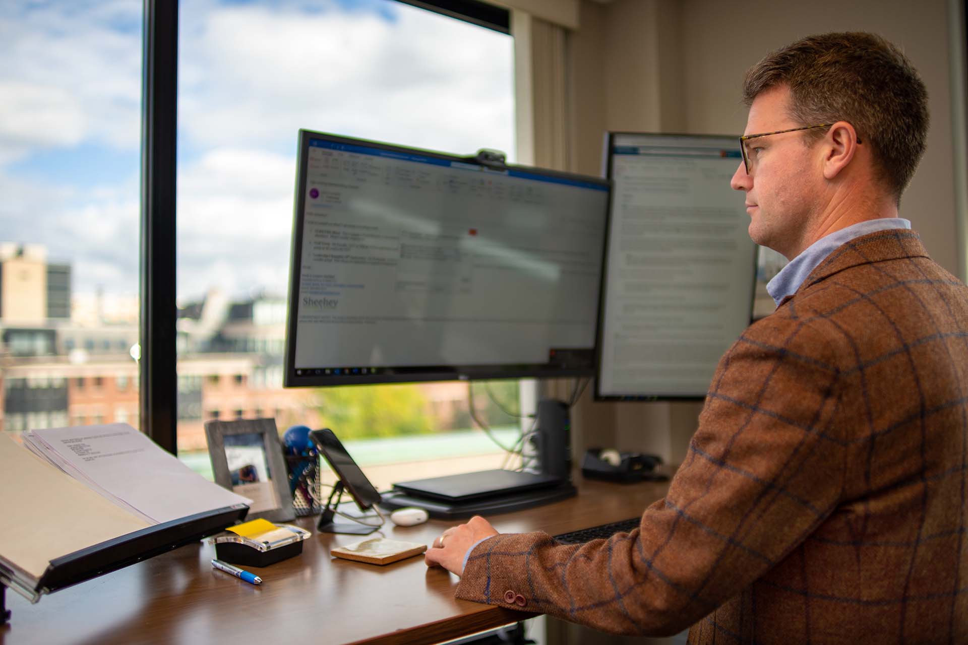 attorney with glasses and blazer sitting at desk emailing on computer