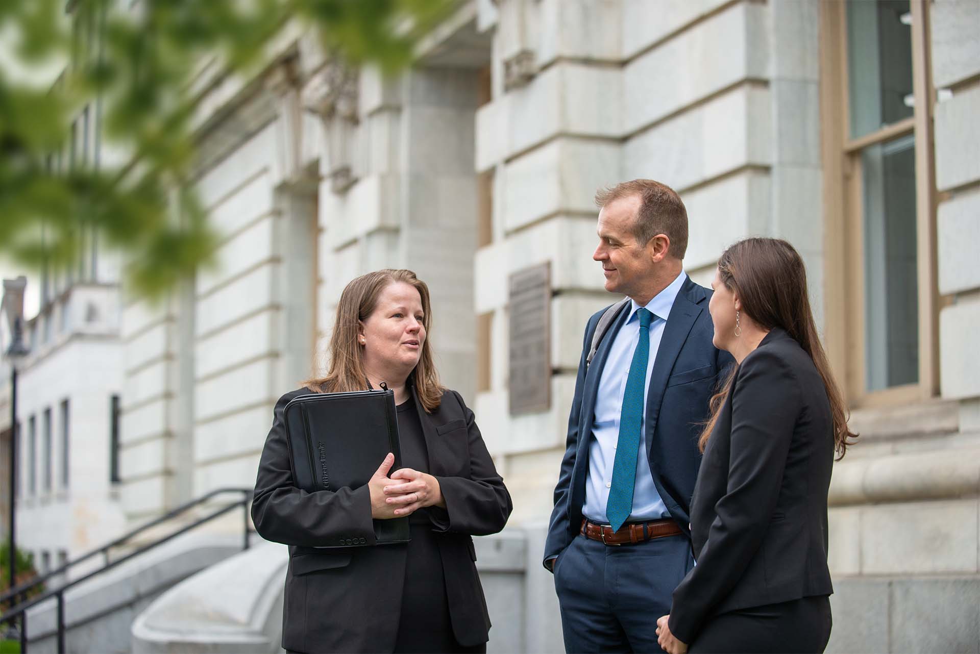 3 people in suits talking outside of courthouse