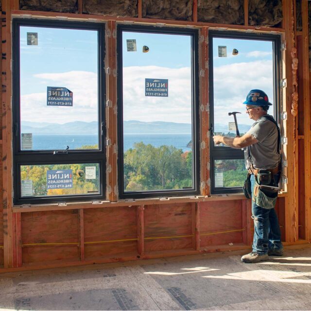 construction worker hammering frame of window that overlooks Lake Champlain