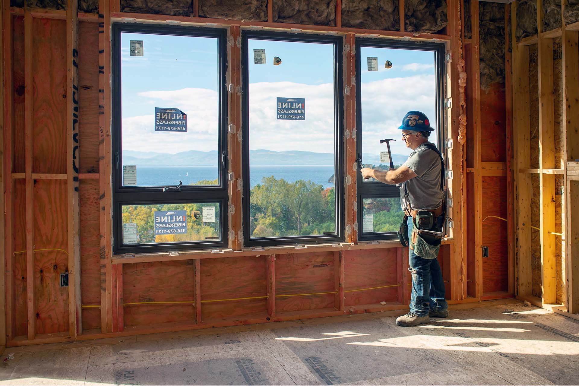 construction worker hammering frame of window that overlooks Lake Champlain